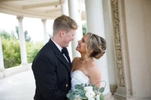 Smiling bride in a strapless white dress holding a succulent bouquet while looking at the groom in a navy military uniform.
