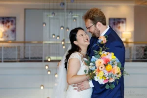 A laughing bride holding a colorful flower bouquet and a groom in a navy suit during a wedding session by Unveiled Wedding Photography.