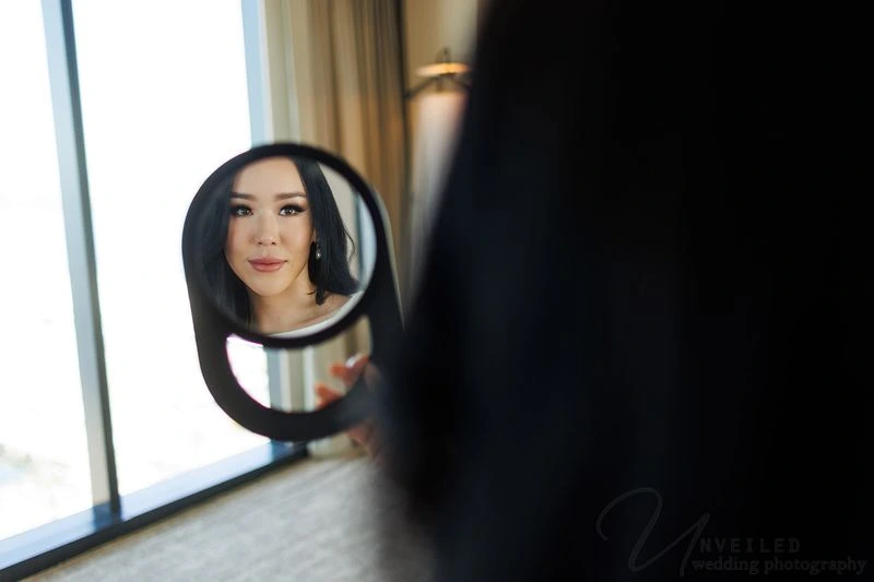 Reflection of a bride looking into a handheld mirror while getting ready for her wedding.