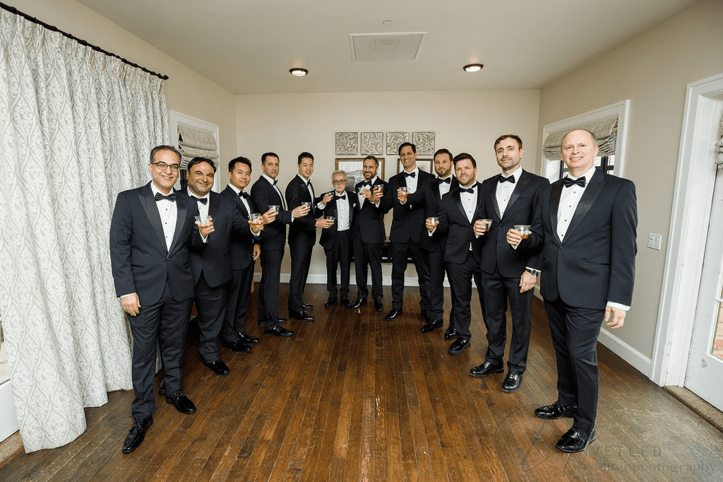 Groom with groomsmen in tuxedos raising drinks indoors, captured by La Jolla Wedding Photographer