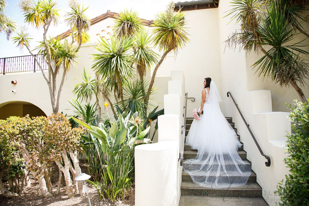 A bride ascends a staircase with her long train and bouquet, taken by a La Jolla Wedding Photographer.
