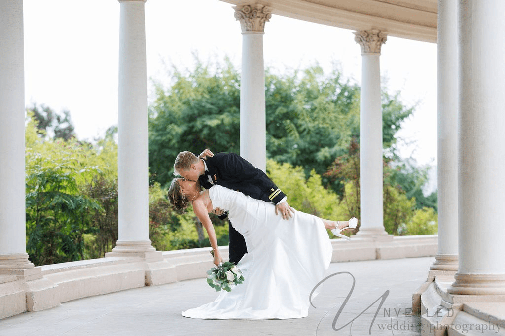 Groom dips and kisses his bride during their San Diego elopement at a scenic white colonnade.