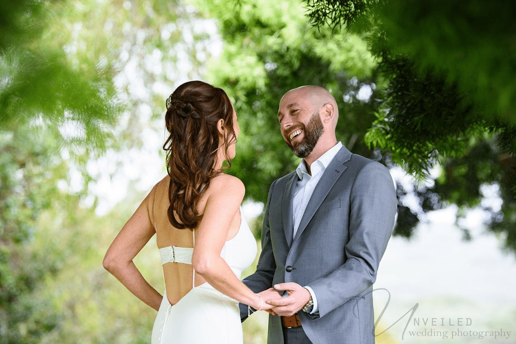 A true-to-life color, heartwarming photo, a joyful groom smiling at his stunning bride, holding hands.