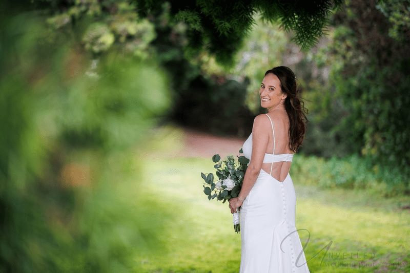 A true-to-life color photograph of a joyful bride in her dress, looking back with a smile.