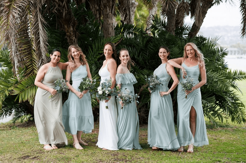 True-to-life color bridesmaids in sage green dresses posing outdoors with bouquets in tropical setting