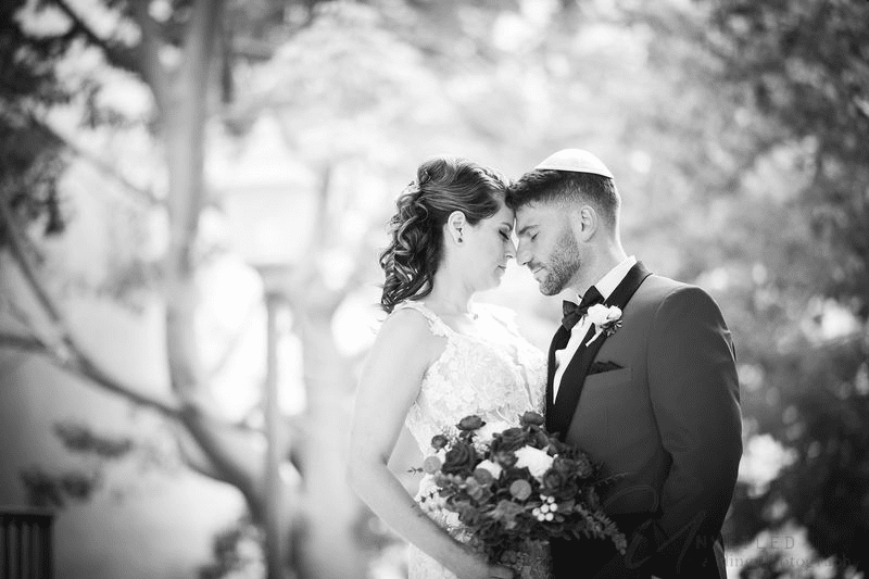 A tender black and white wedding portrait of a bride and groom touching foreheads with closed eyes.