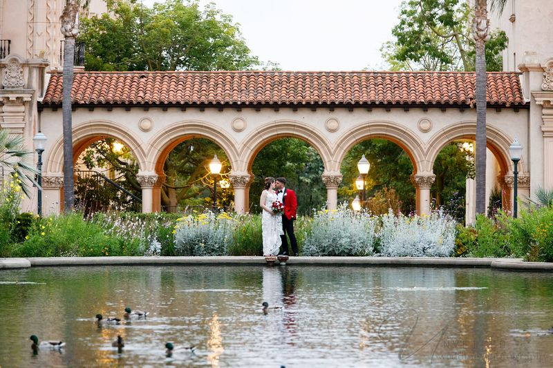 Elegant wedding couple standing by a pond in lush garden before arched building at sunset serene vie