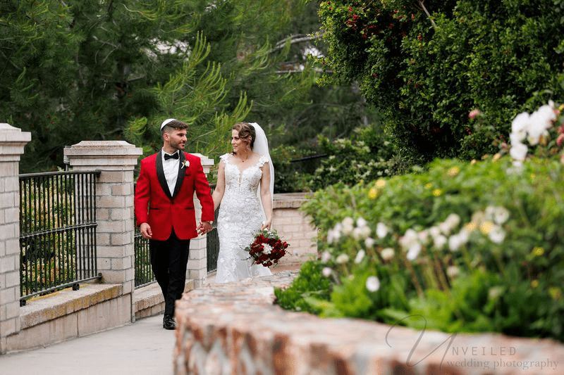 A wedding couple sharing a kiss on a balcony with palm trees and Mediterranean architecture.