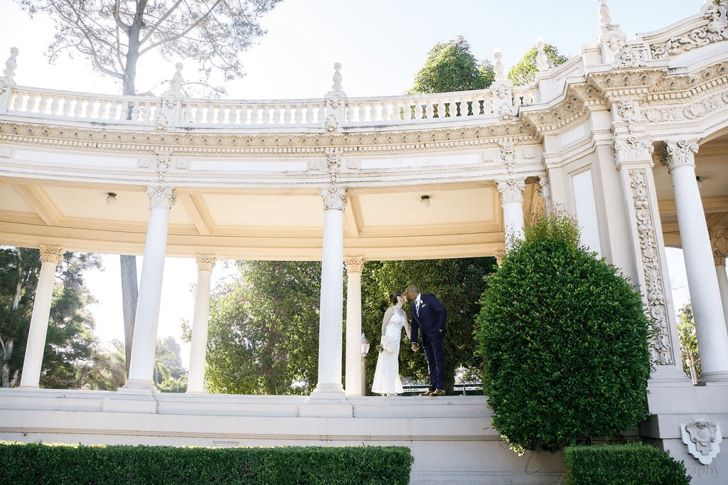 A couple kisses under a stone colonnade for San Diego Courthouse Wedding Photography.