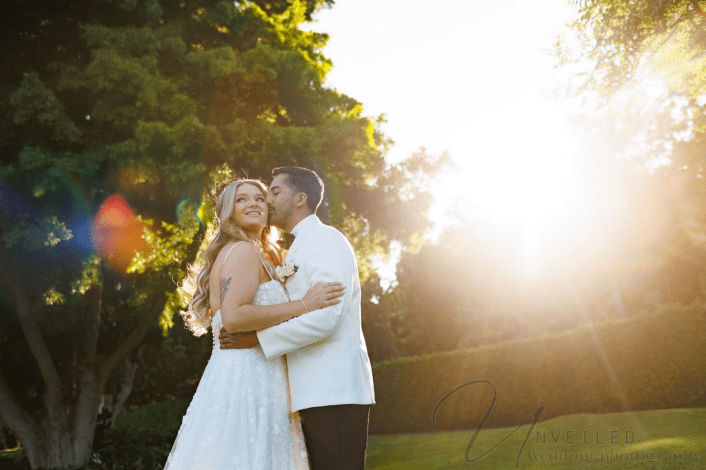 Golden Hour Wedding Photos of a groom kissing a bride's cheek outdoors with warm sunlight.