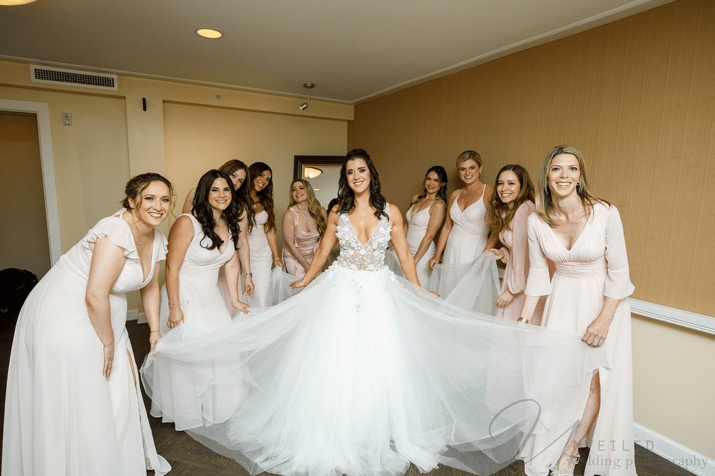 Bride with bridesmaids holding her gown indoors, joyful moment captured by La Jolla Wedding Photographer