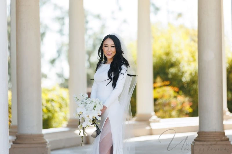 A portrait of a bride in a long-sleeved white gown and veil, holding a white orchid bouquet.