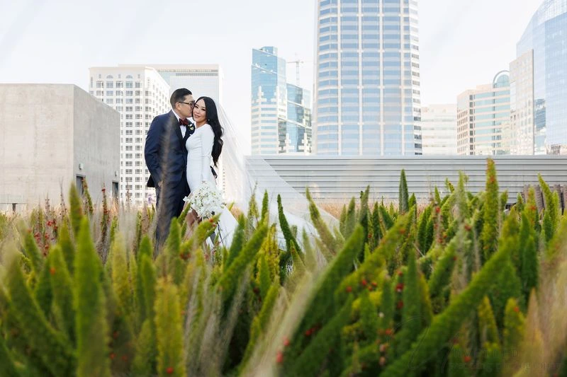 A bride and groom sharing a kiss while standing beside elegant classical stone columns.