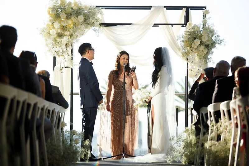 
A wedding ceremony with a couple at the altar and an officiant speaking under a floral arch.