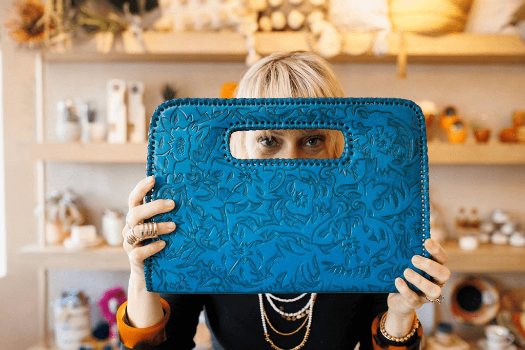 A woman looking through the handle of a blue, embossed leather clutch purse.