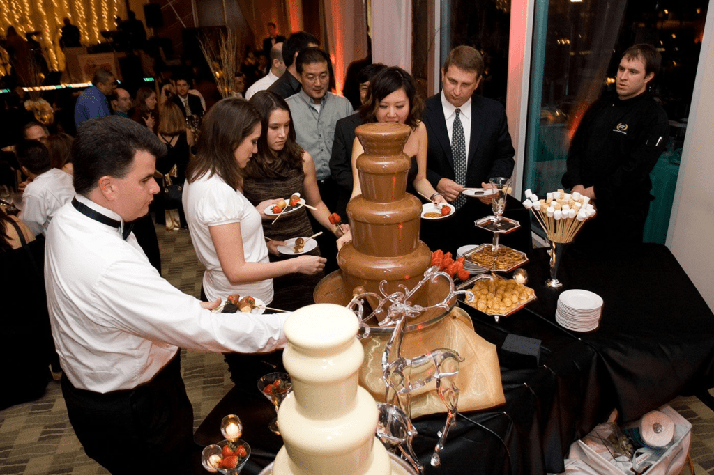 Guests gathering around a multi-tiered chocolate fountain at a formal indoor event.