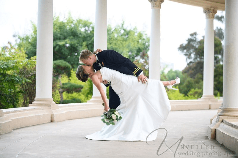 Wedding couple smiling under veil during outdoor ceremony