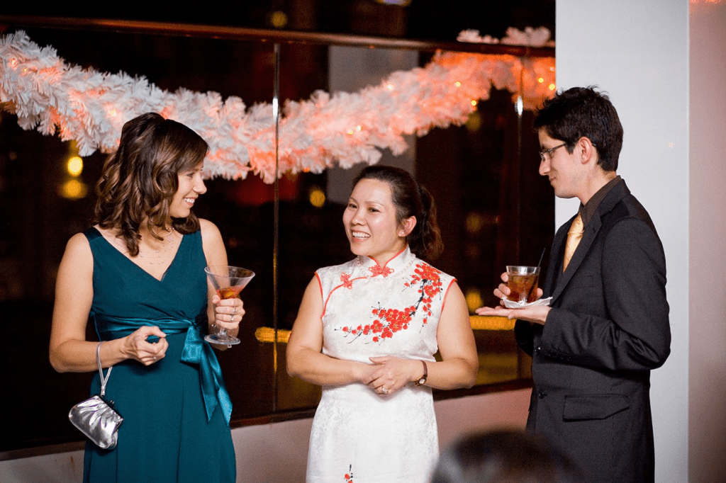 Three people in formal attire talking and holding drinks at an evening gathering.