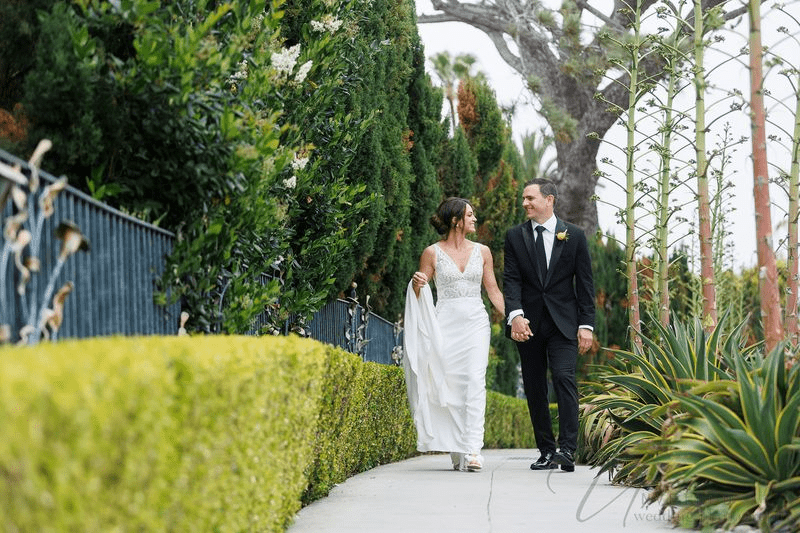 A bride and groom sharing a laugh while standing under an umbrella during a rain shower.