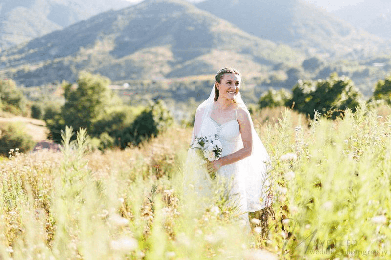 A bride and groom sharing a romantic kiss outside in front of a stone building.