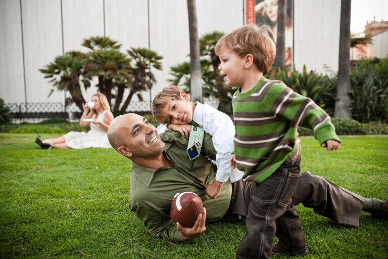 A father playing with his two sons on the grass while holding a football.