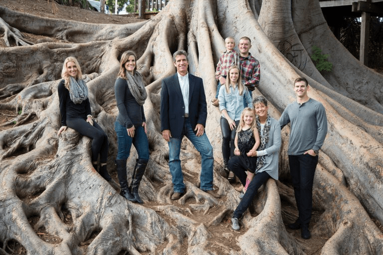 A family posing for a portrait among the large, sprawling roots of a tree.