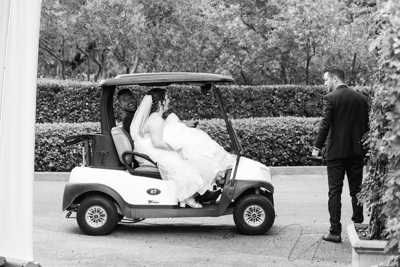 Black and white photo of a bride sitting in a golf cart at her wedding.