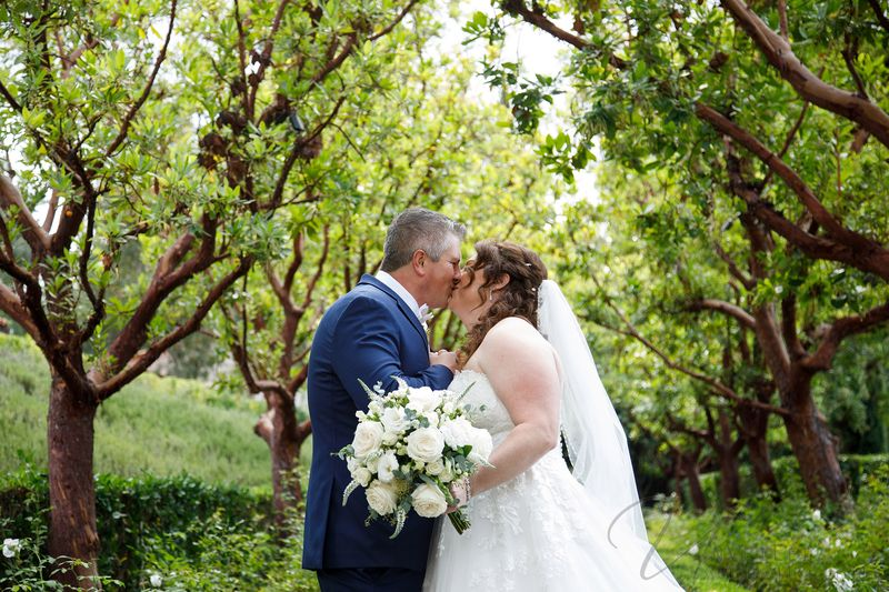 Bride and groom kissing in a lush green garden at their outdoor wedding.