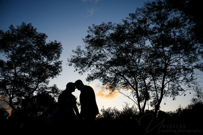 Silhouette of a bride and groom touching foreheads during a sunset wedding.