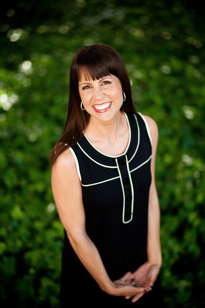 San Diego corporate headshots of a professional woman in a grey blazer smiling outdoors with a blurred natural background.