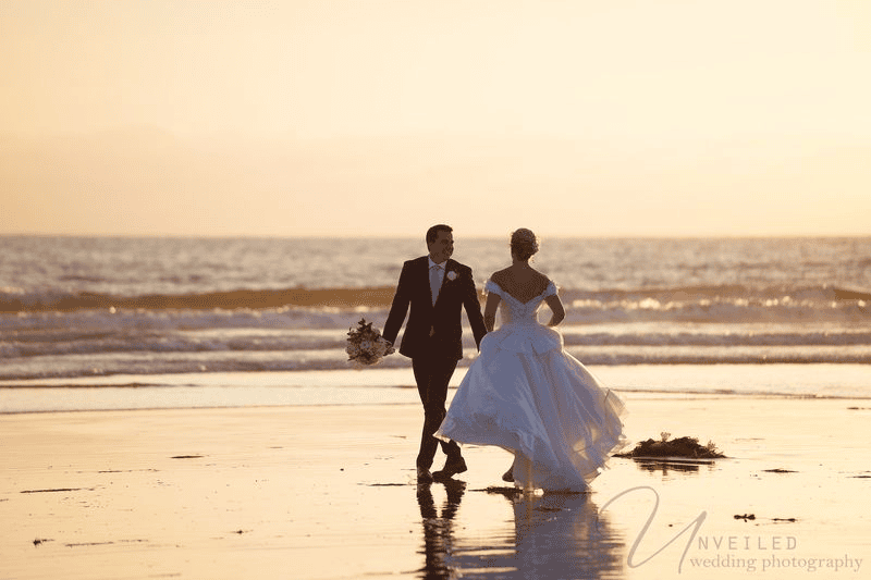 Bride and groom walking on beach at sunset for Wedding Photography Contract.