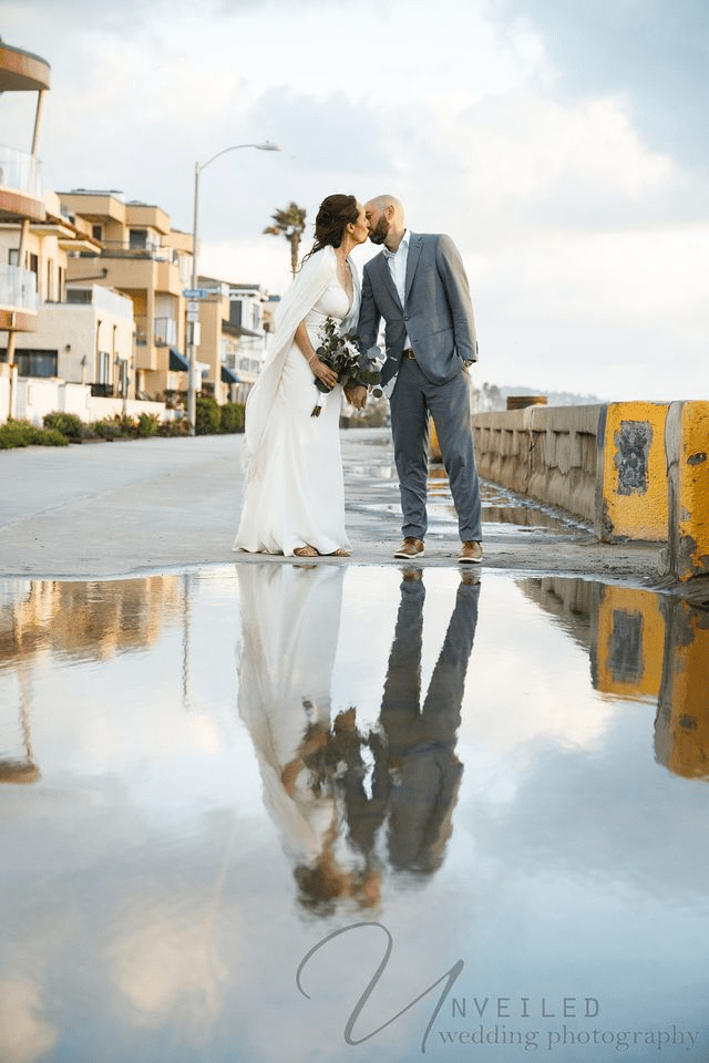 Newlyweds kissing near beachfront properties with a unique water reflection.
