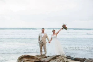 Bride and groom standing on rocks by ocean: inspiration for Sunset Cliffs elopement photos.