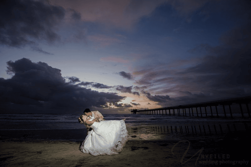 Groom dipping bride on beach at sunset: stunning Sunset Cliffs elopement photos.