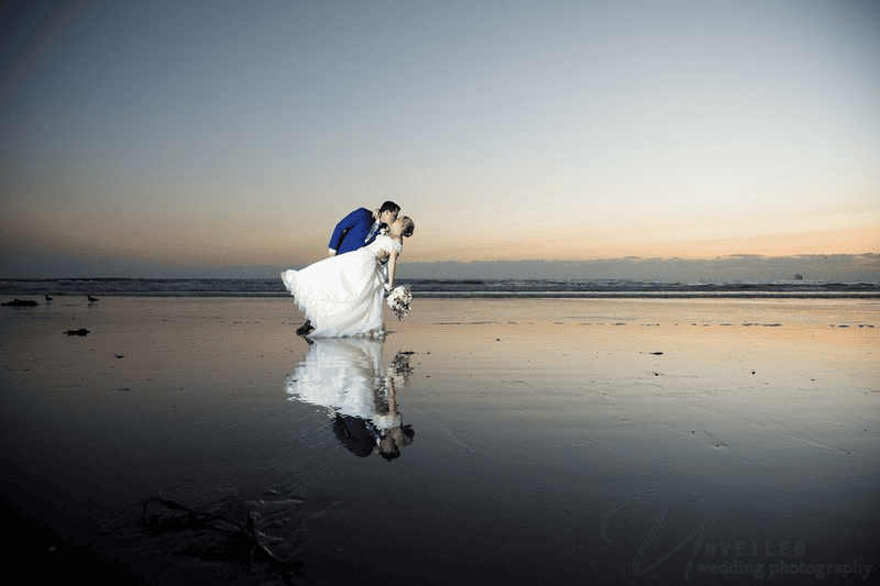 Groom dipping bride for sunset kiss with water reflection: intimate wedding in San Diego.