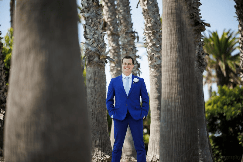 Groom in blue suit standing among palm trees during an intimate wedding in San Diego.