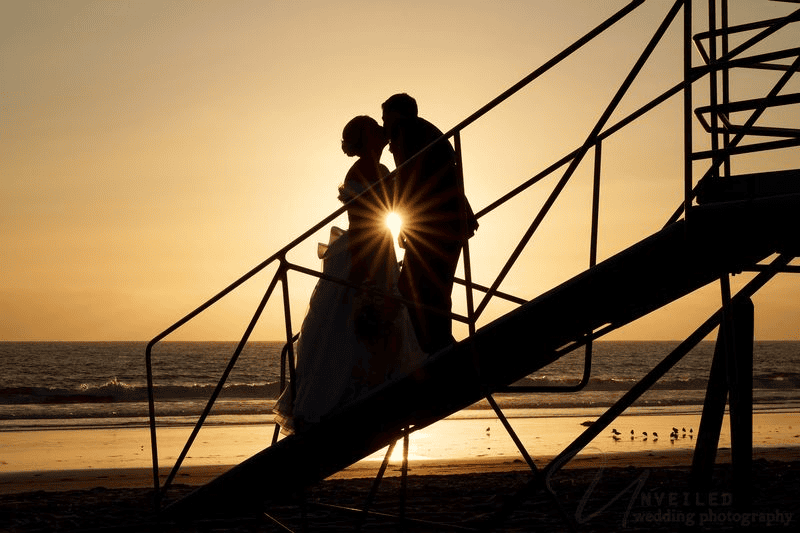 Sunset silhouette kiss on lifeguard tower stairs: intimate wedding in San Diego.