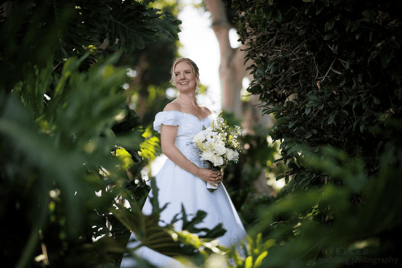 Bride holding flower bouquet surrounded by garden greenery: intimate wedding in San Diego.