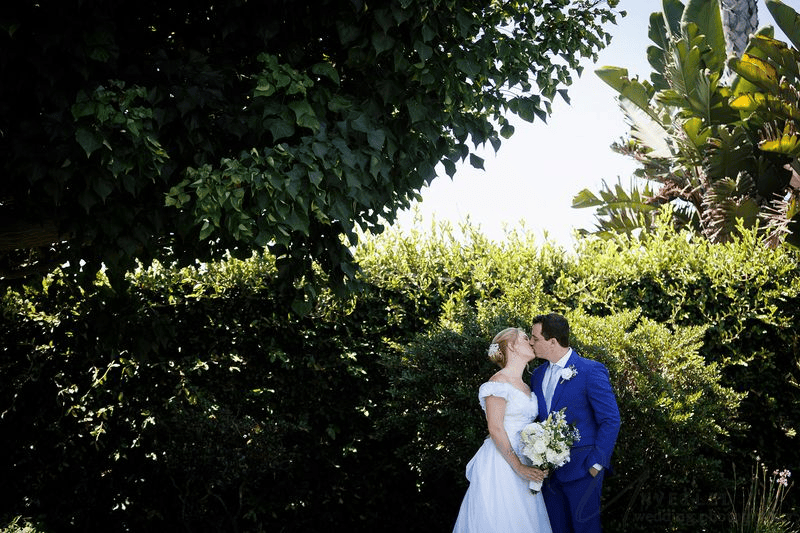 Bride and groom kissing amidst tropical garden foliage: intimate wedding in San Diego.
