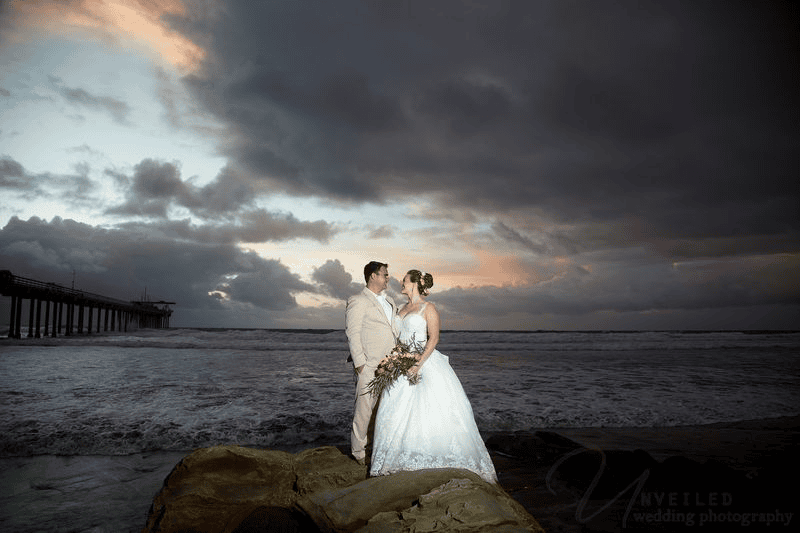 Bride and groom standing near ocean at sunset: beautiful Sunset Cliffs elopement photos.