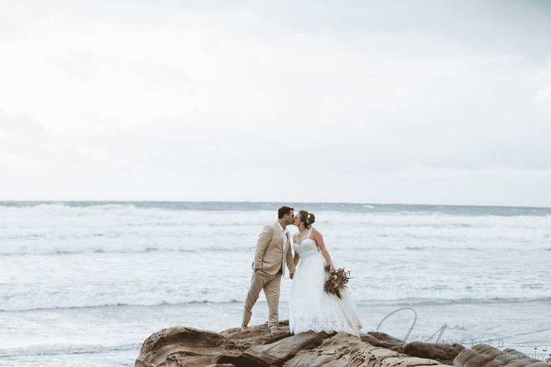 Bride and groom kissing on coastal rocks: beautiful Sunset Cliffs elopement photos.