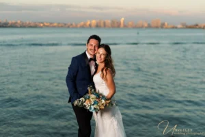 Smiling bride and groom posing by oceanfront during Wedding Photography Coverage.