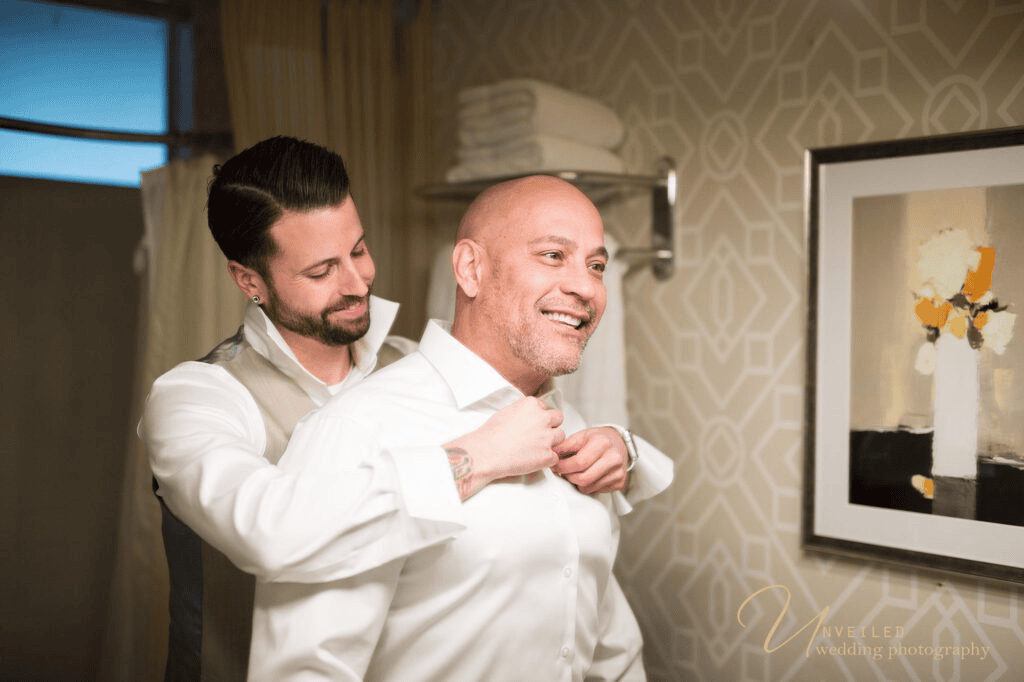 Groom helping partner get dressed shot by same-sex wedding photographer in San Diego.