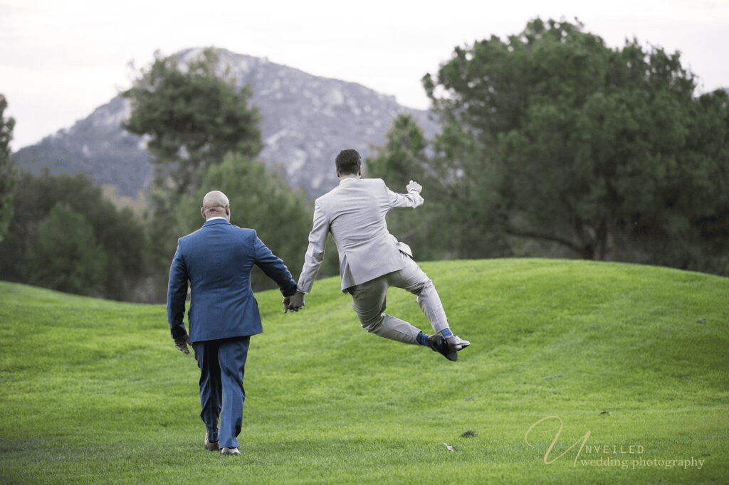 Groom jumping in joy while holding hands by same-sex wedding photographer in San Diego.