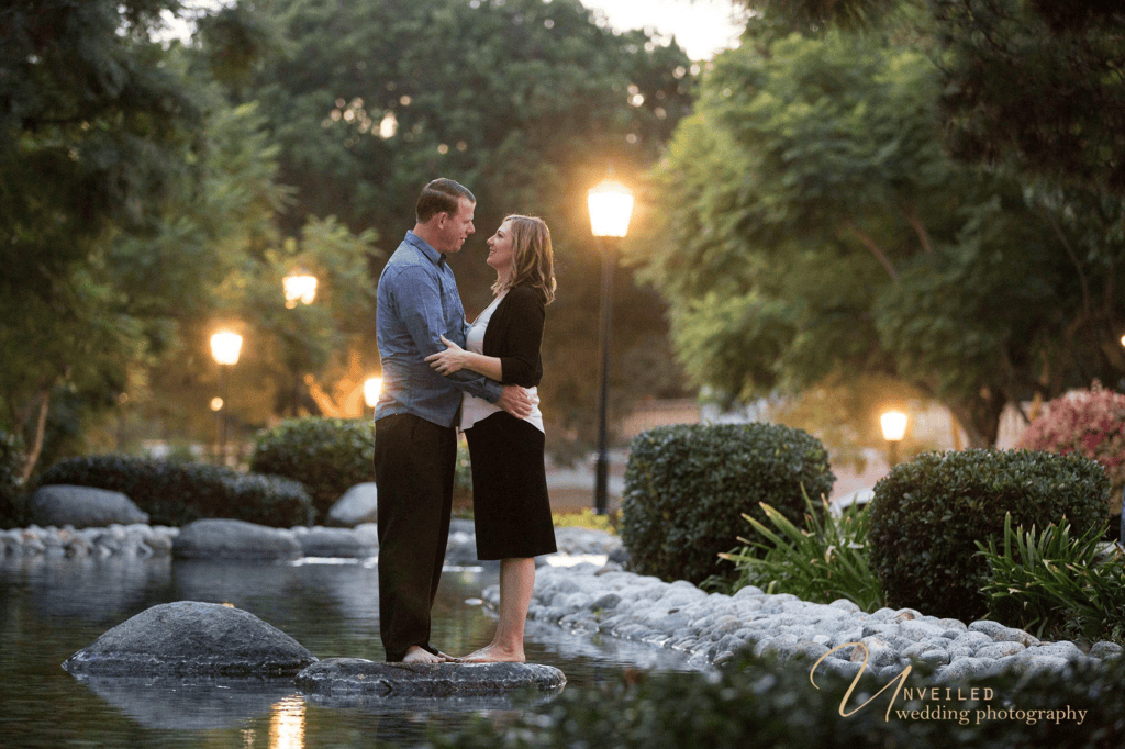 Couple embracing by park pond at dusk for an engagement session before your wedding.