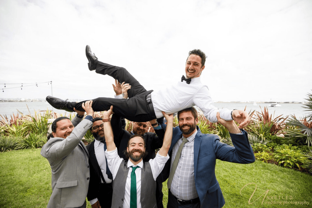 Groomsmen lifting groom in air outdoors during Wedding Photography Coverage.