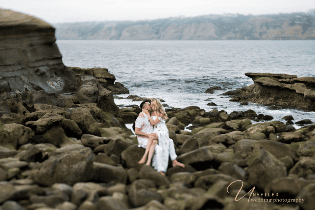 Couple kissing on rocky beach shore for an engagement session before your wedding.