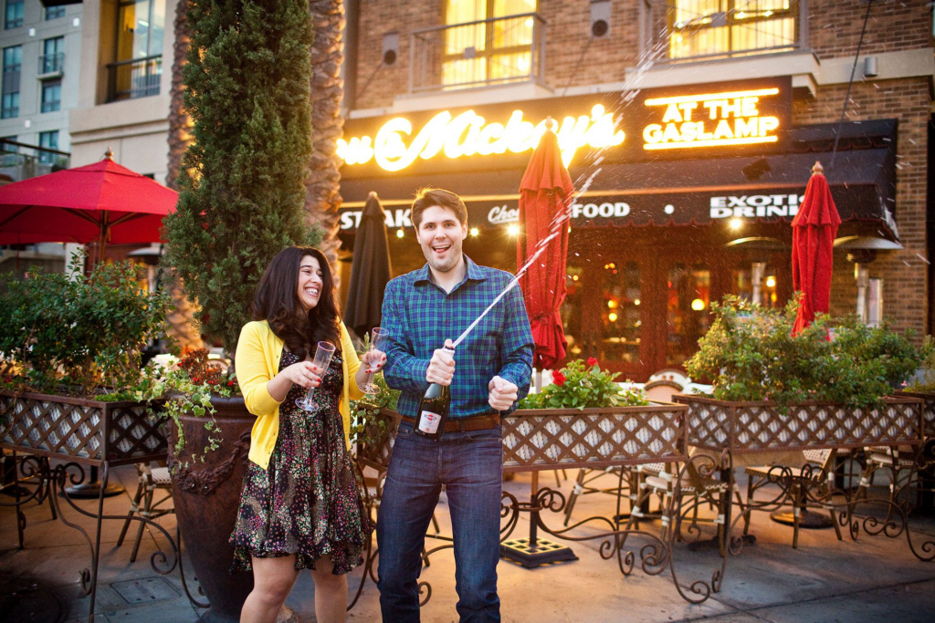 Couple popping champagne outside restaurant for engagement session before your wedding.