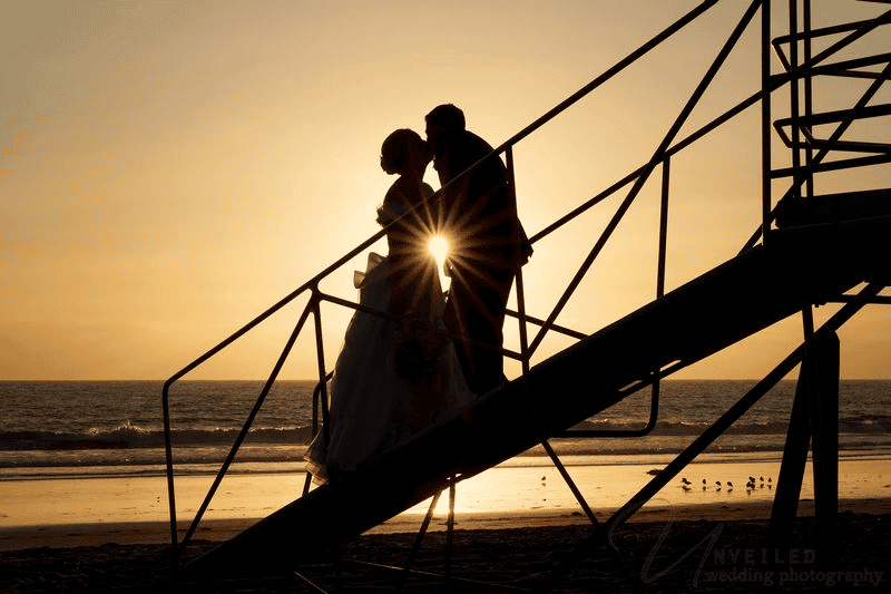 Sunset silhouette kiss on beach stairs capturing Wedding Photography Trends 2027.