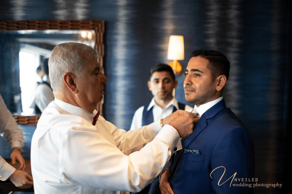 Groom getting tie adjusted by family during prep for Wedding photography shots.